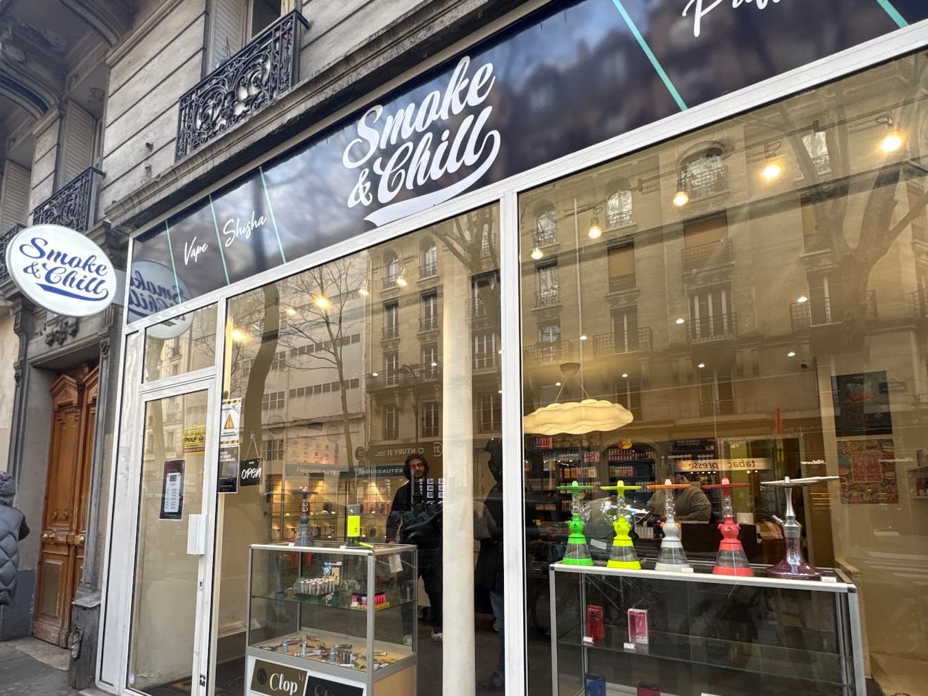 Le magasin Smoke & Chill vu de l’avenue Simon Bolivar : bandeau anthracite, logotype script et vitrine blanche